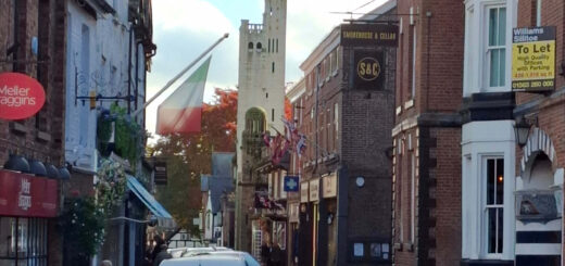 A square asymmetrical tower at the end of a narrow street of shops