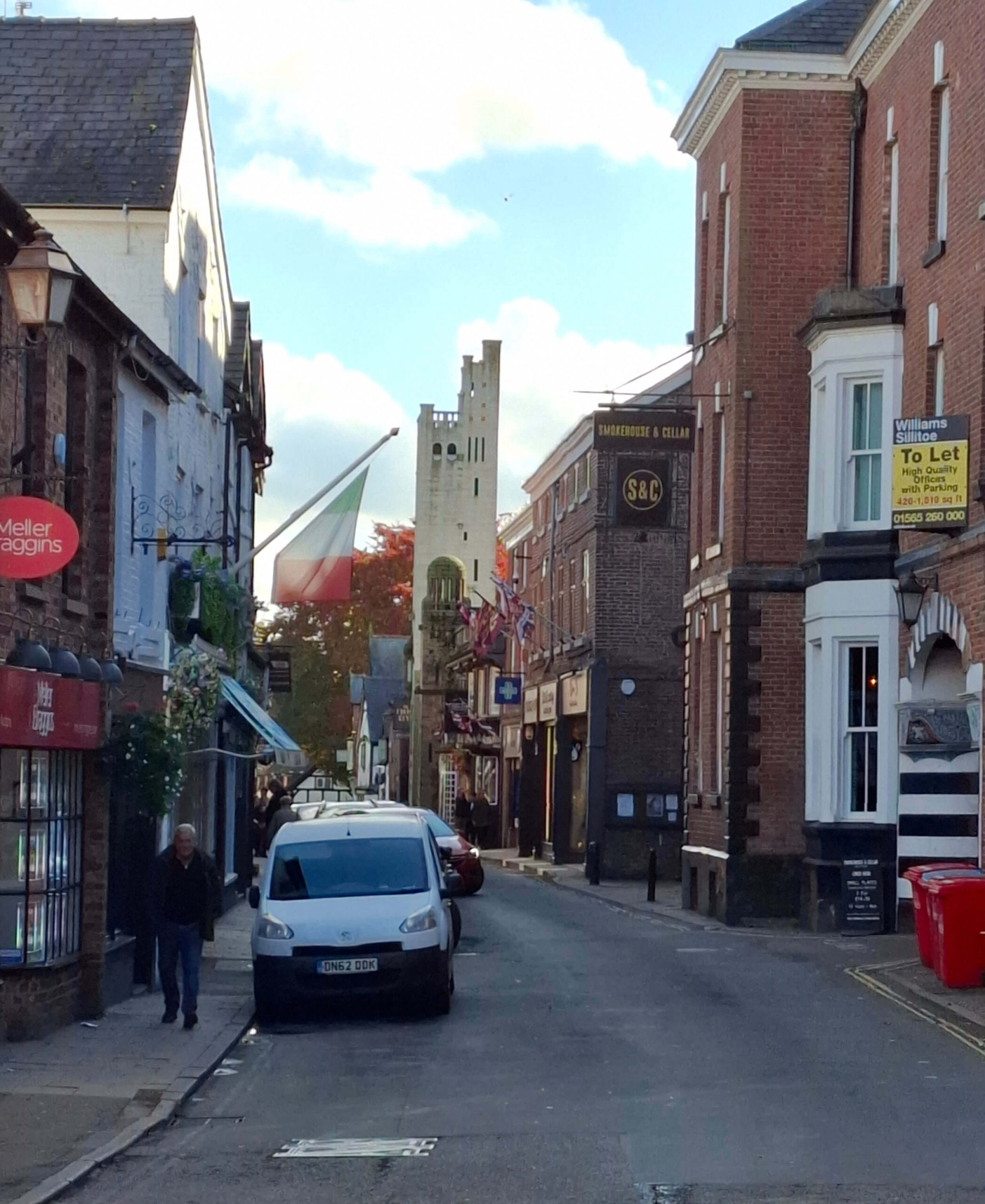 A square asymmetrical tower at the end of a narrow street of shops