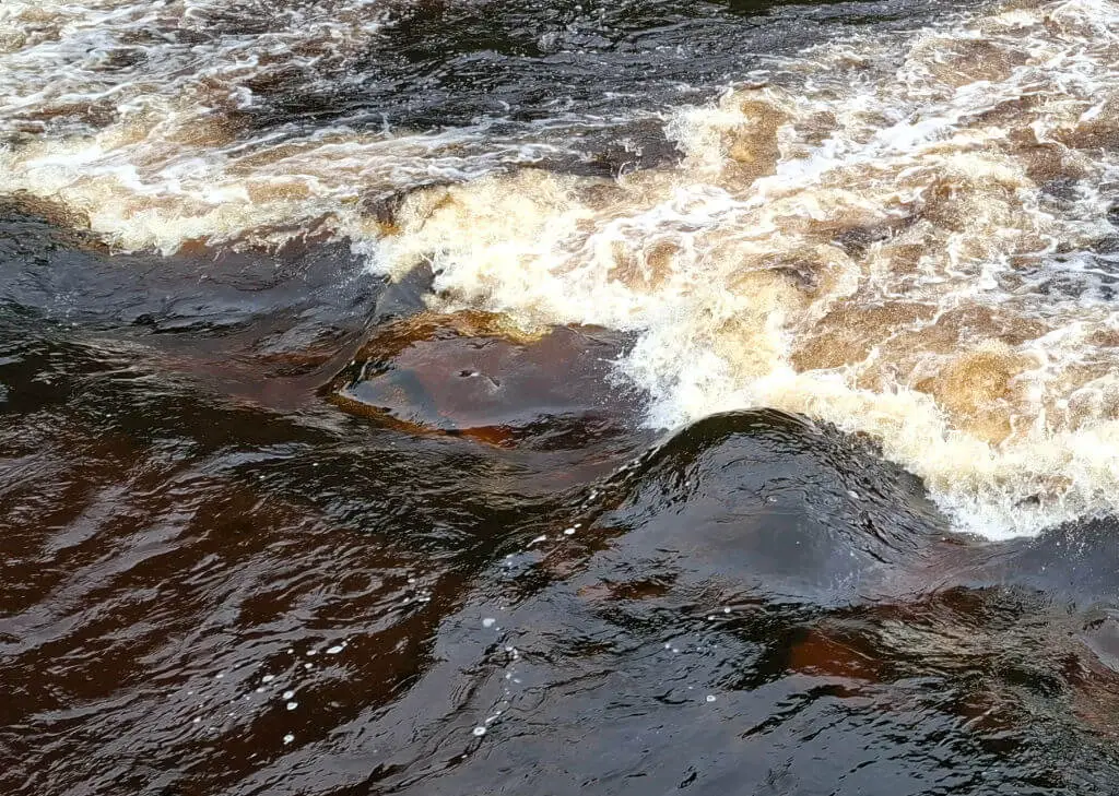 A close up of brown river water as it tumbles over rocks