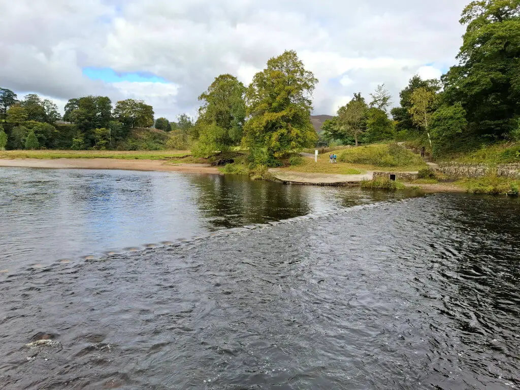 Stepping stones breaking up the smooth flow of water in a river.  The stones are partly submerged and after the water meets the stones, the water is choppy