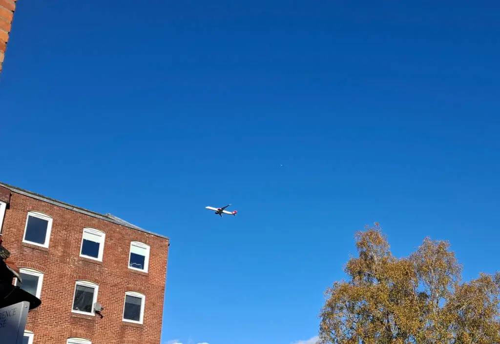 An aeroplane in a cloudless blue sky above a square office building