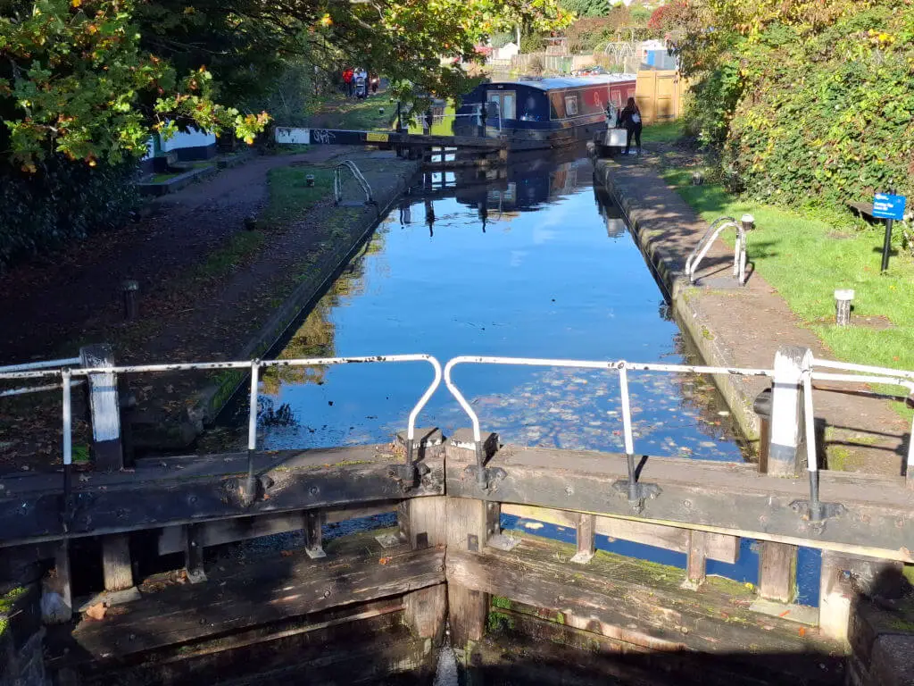 A narrowboat at the far end of a canal lock, moving closer to the lock gates