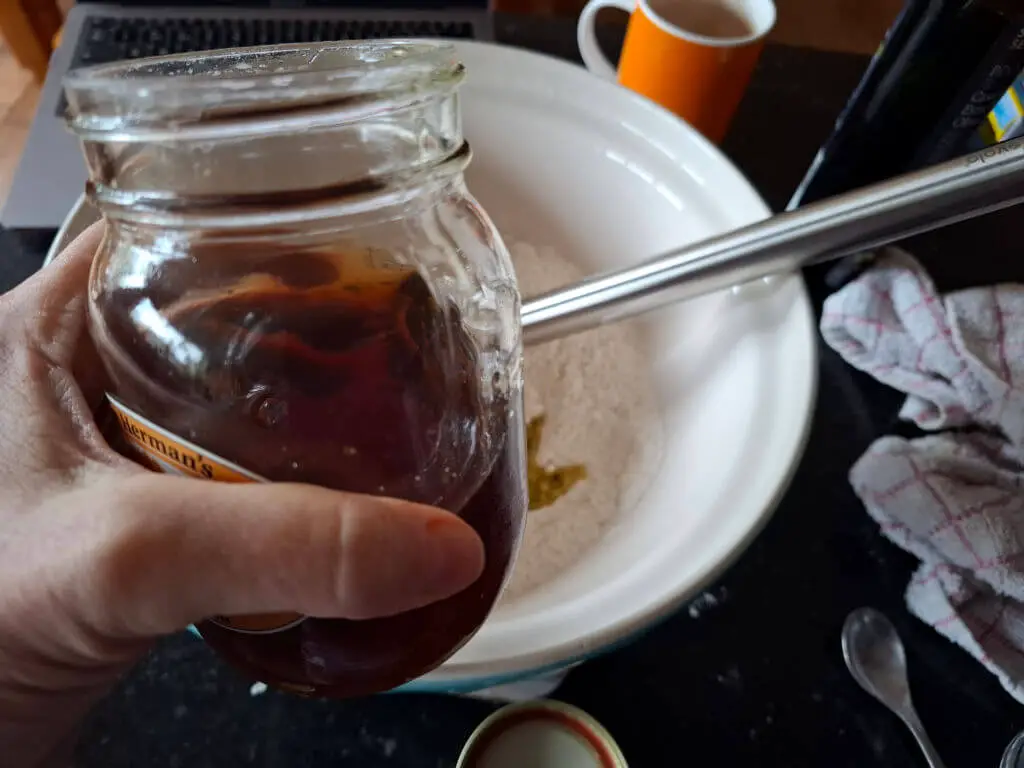 A hand holding a jar of maple syrup over a mixing bowl