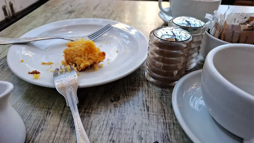 The remains of a slice of cake and two forks on a white plate, next to salt and pepper pots on a cafe table