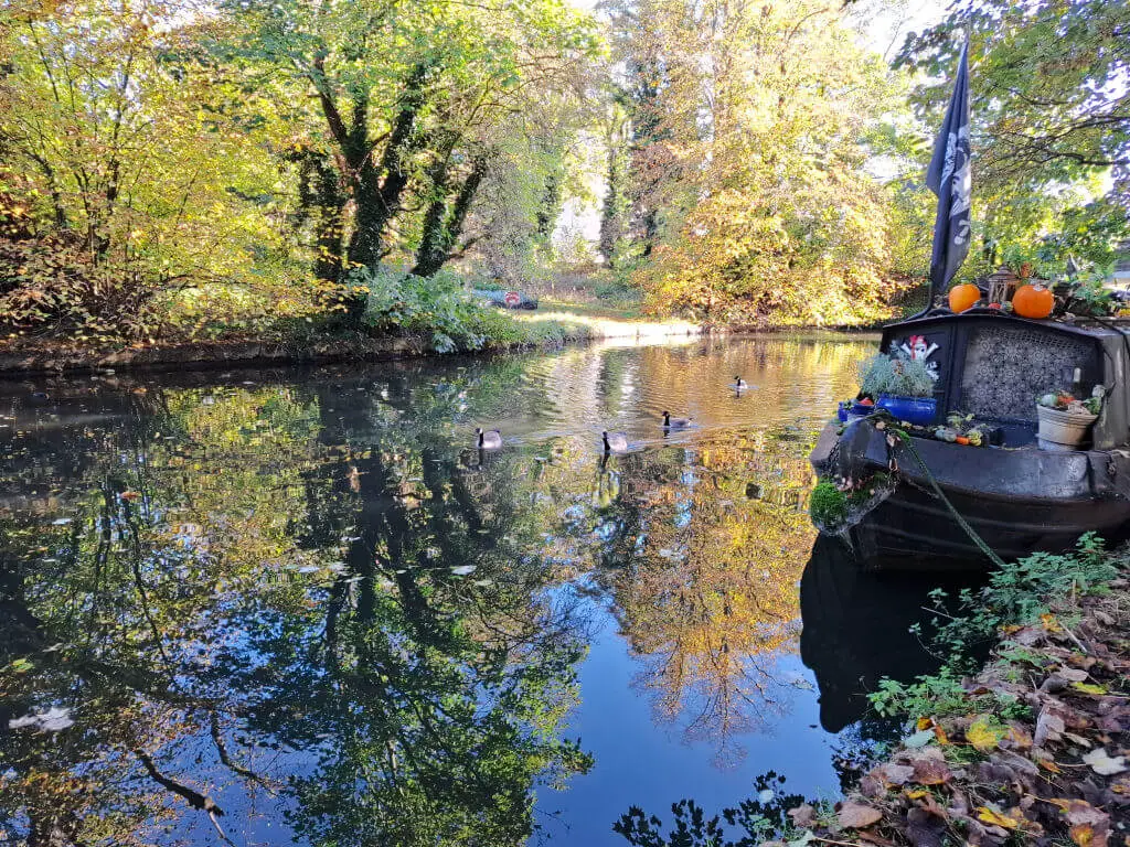 Reflections in the water of a canal. There is a black narrowboat in the water and trees lining the banks