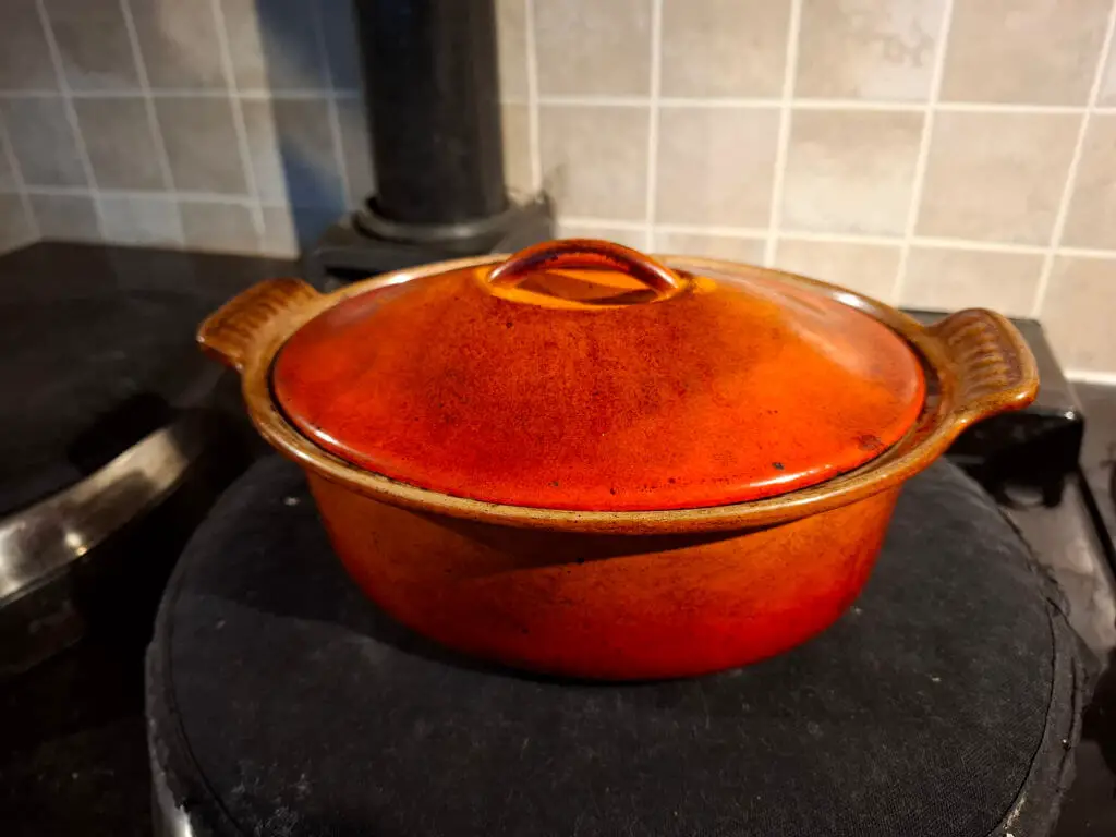 A orange cast iron casserole dish standing on an Aga lid