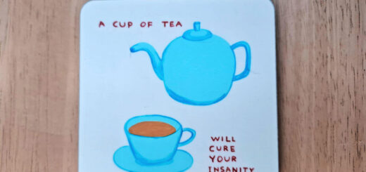 A square white coaster with rounded edges, with a picture of a blue teapot and cup and saucer on it. The words on the coaster are "A cup of tea will save your sanity"