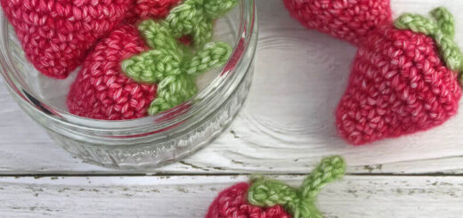 A glass jar on a white wooden painted board containing crochet strawberries