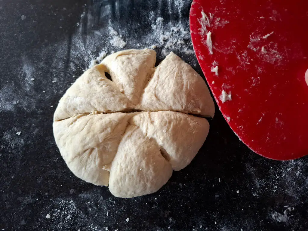 A circle of dough cut into six sections by a red plastic dough scraper