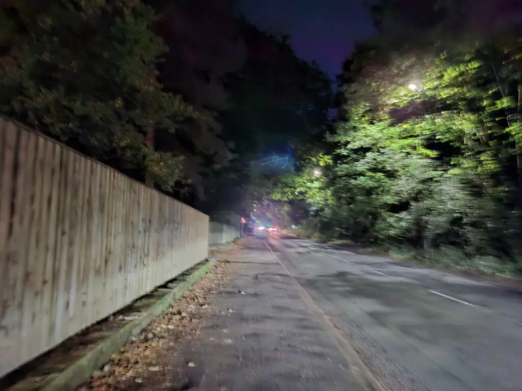 A dark street lit up by car headlights behind the photographer
