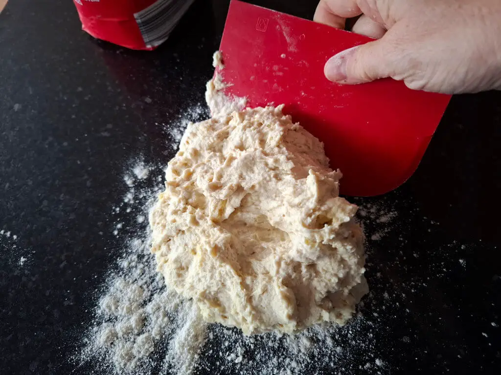 A sticky dough mess stuck to a working top and a red dough scraper