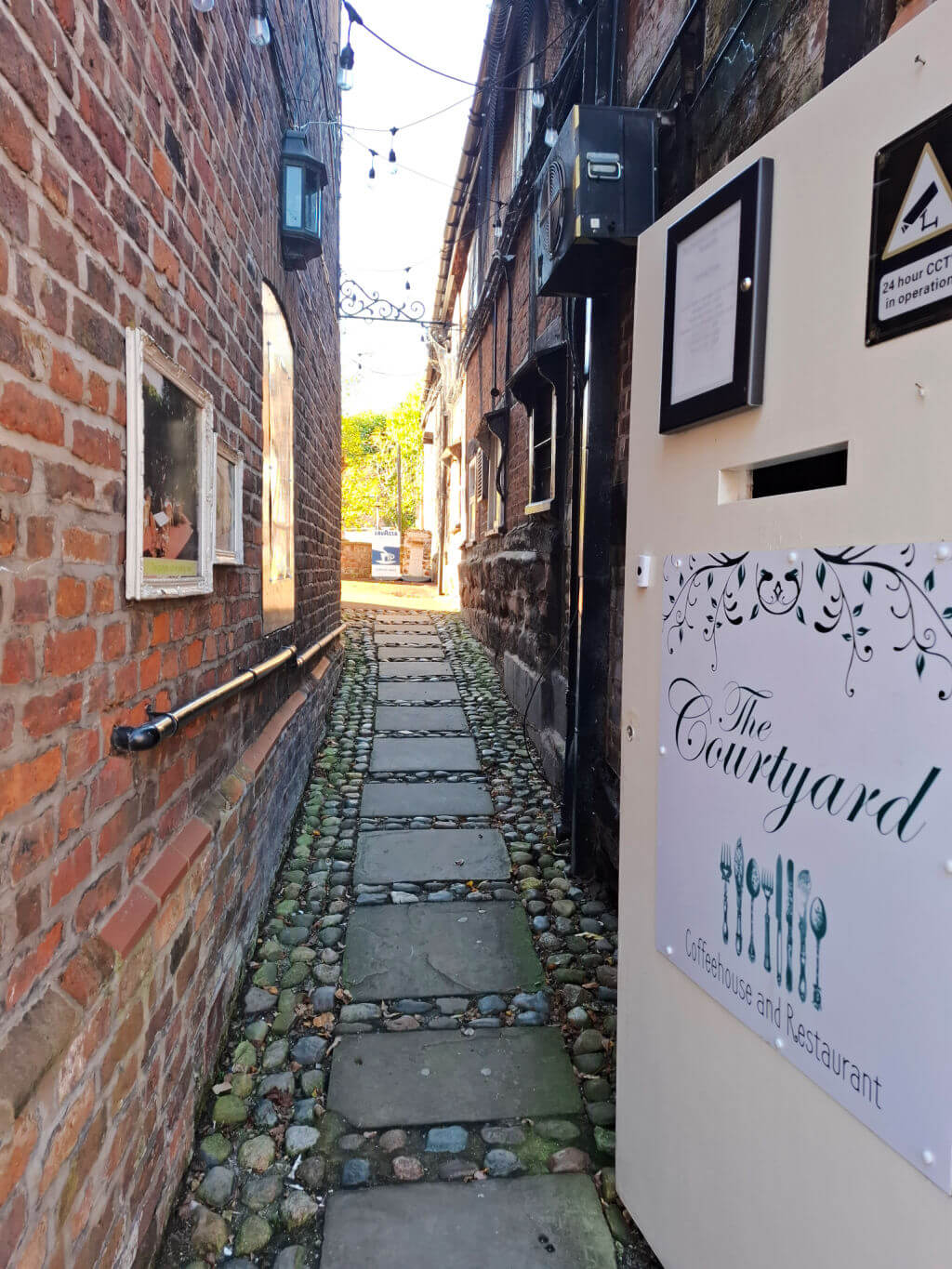 A narrow paved and cobbled entrance to a cafe