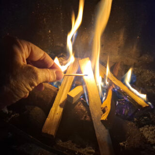 A hand holding a match to start a fire. There are already flames around the kindling