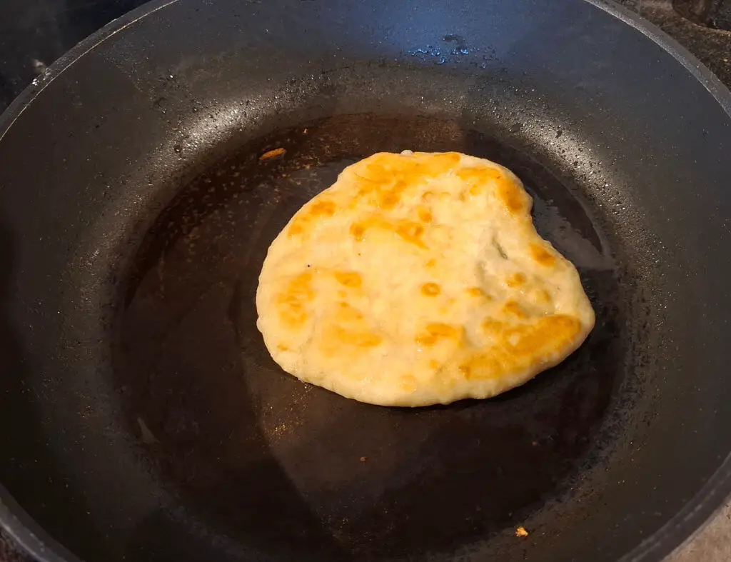 A round-ish flatbread cooking in a frying pan