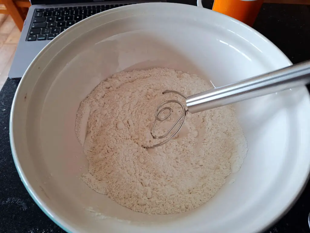 A mixing bowl of flour with a hand whisk resting on the flour