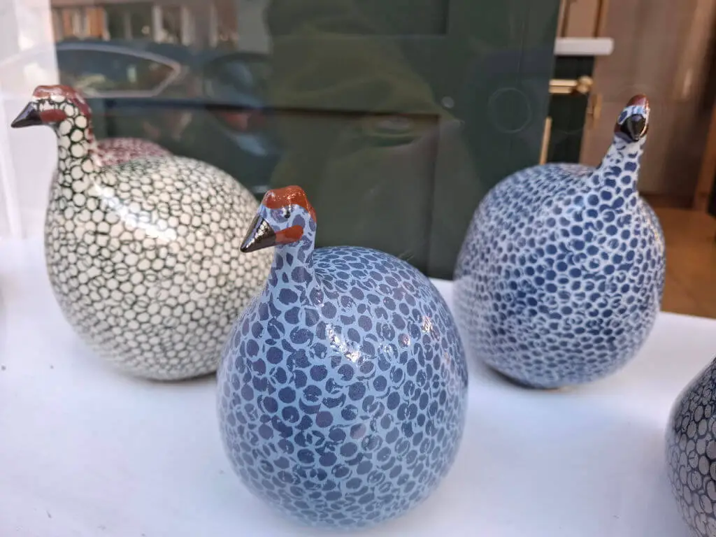 A close up of three pottery guinea hens in a shop window. Two are blue and one is grey