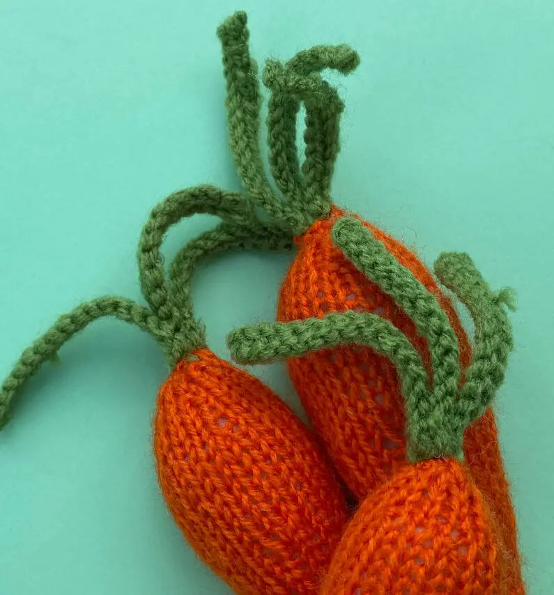 Three knitted carrots on a green background