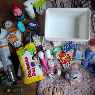 A big pile of travel plugs, sun cream bottles, face flannels and other toiletries on a pink furry rug next to an empty white storage box