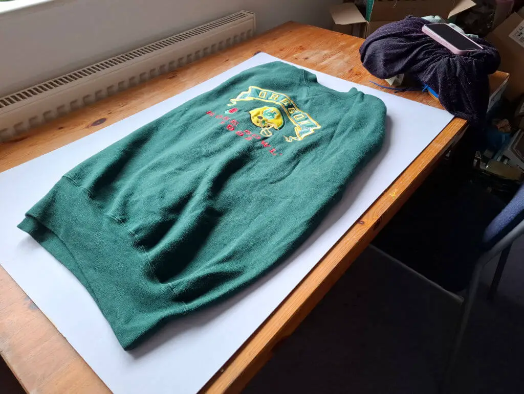 A green sweatshirt folded up on a cardboard photography board on a wooden table