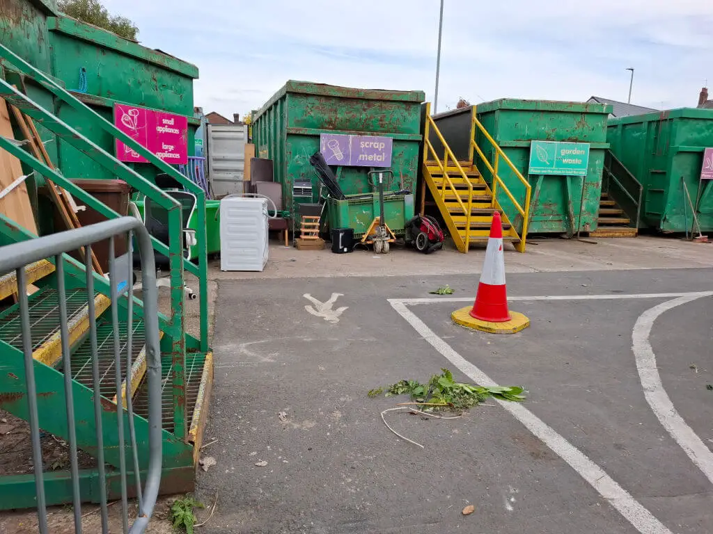 Bright green skips in a line at a council tip, each one labelled with the items that are allowed to be put into each one