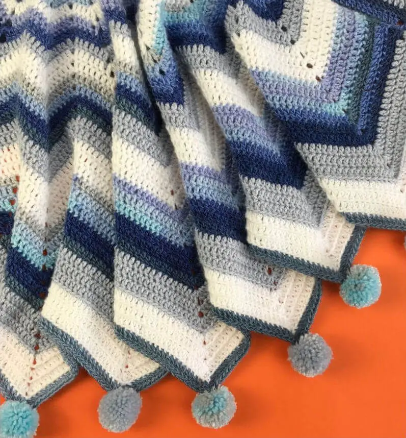 A star-shaped crochet baby blanket in stripes of white, grey, navy and sky blue on an orange background