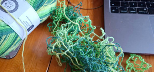 Unravelled green yarn on a wooden table next to an open laptop and the rest of the ball of yarn