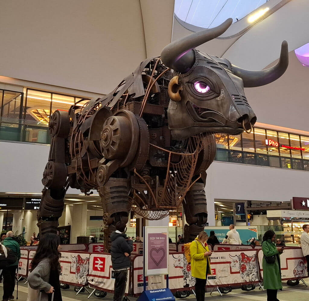 A giant metal bull sculpture with purple eyes in a railway station 