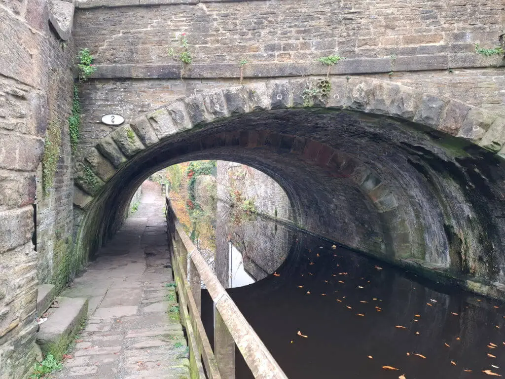 A low arched stone bridge across a canal. The towpath goes under the arch at the lowest point