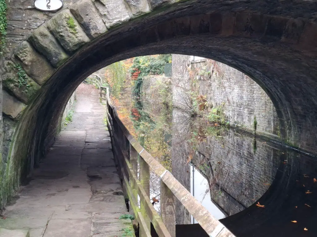 A close up of reflections in the water of a canal under a low arched bridge