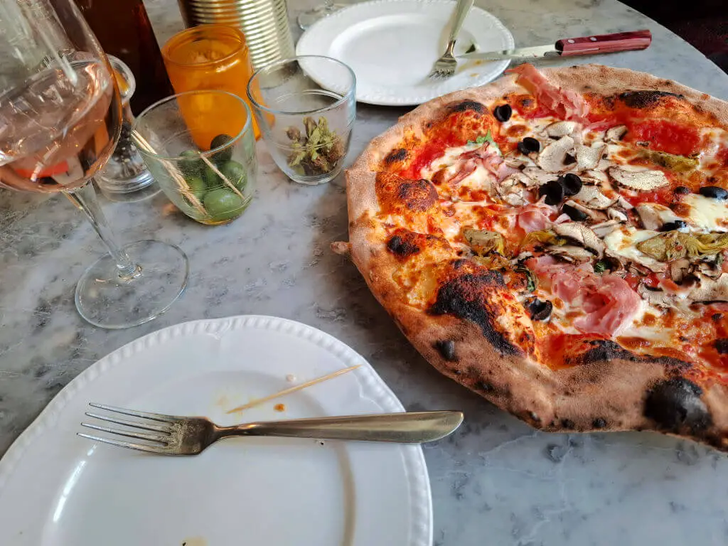 A large pizza ready to be shared, and two plates and glasses of wine on a table