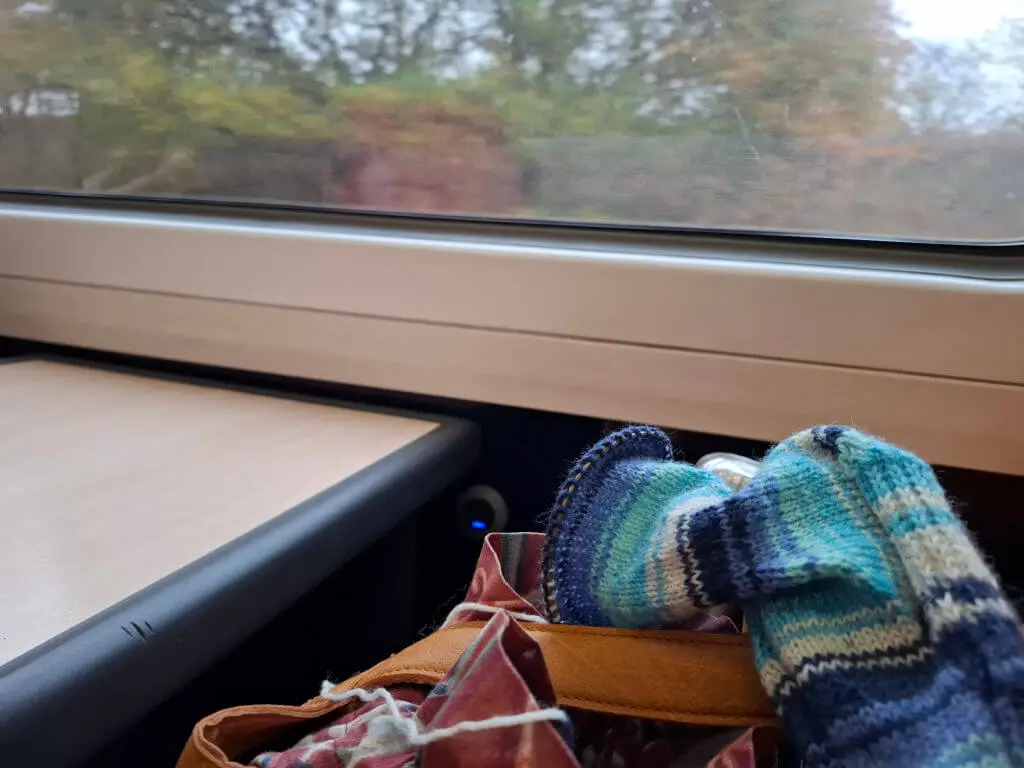 A partly knitted blue-striped sock on a leather bag on a train