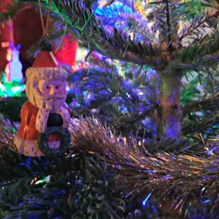 A small Santa ornament sitting amongst the boughs and tinsel of a real Christmas tree