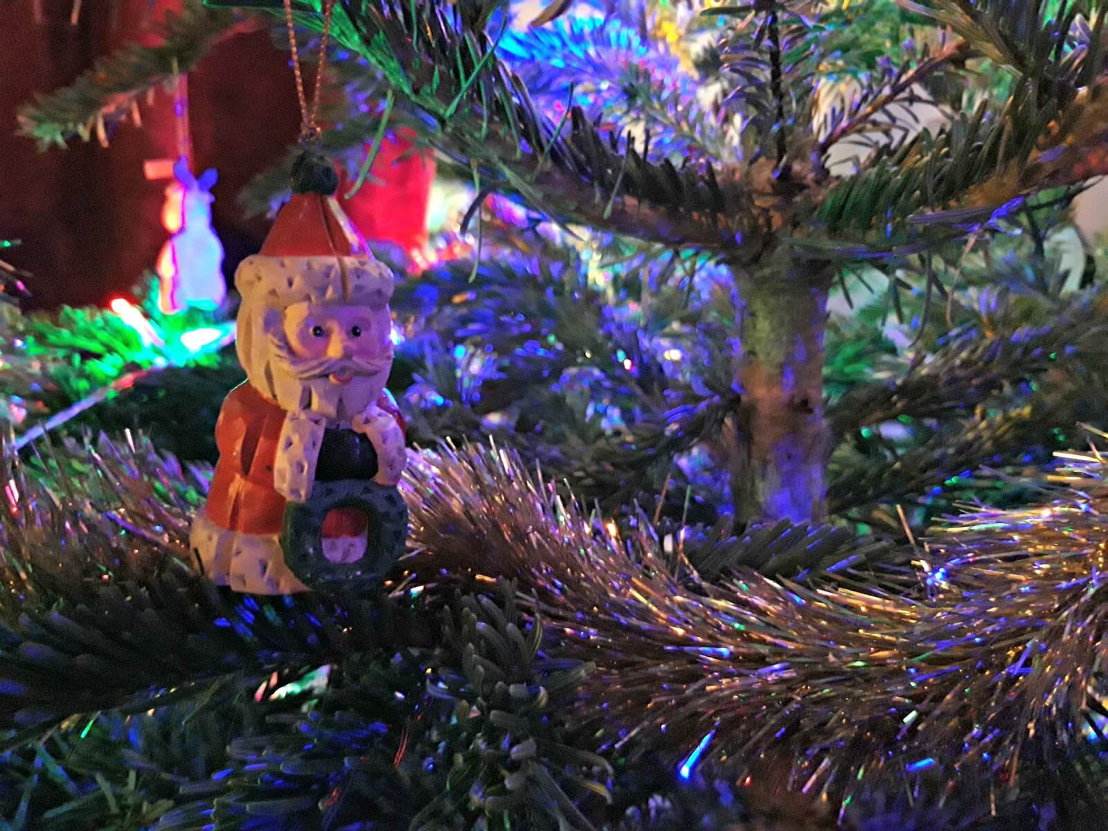 A small Santa ornament sitting amongst the boughs and tinsel of a real Christmas tree