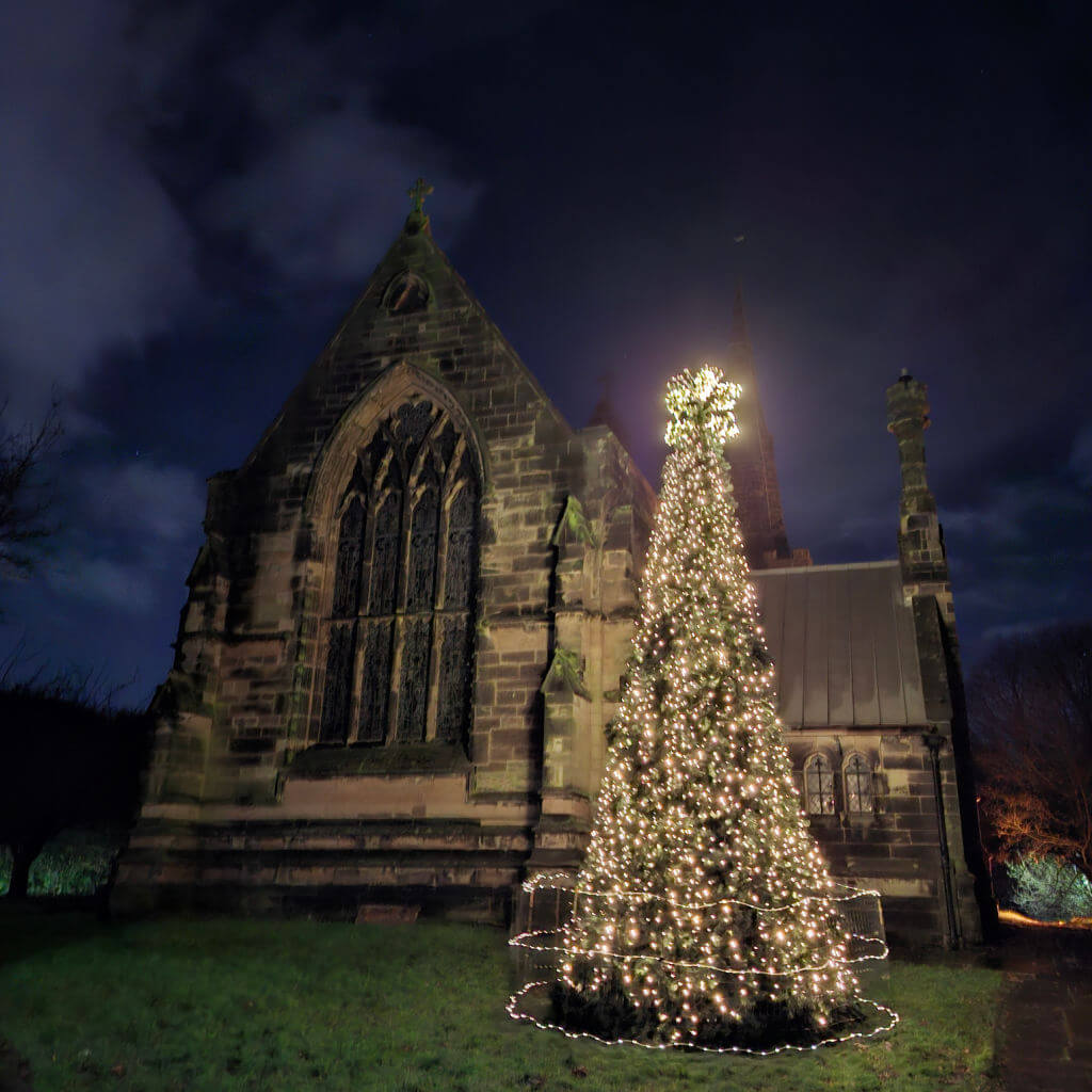A Christmas tree covered with lights outside a church