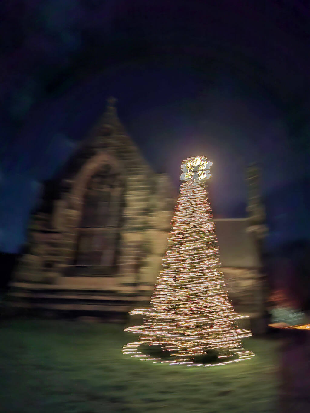 A blurred photo of a Christmas tree outside a church