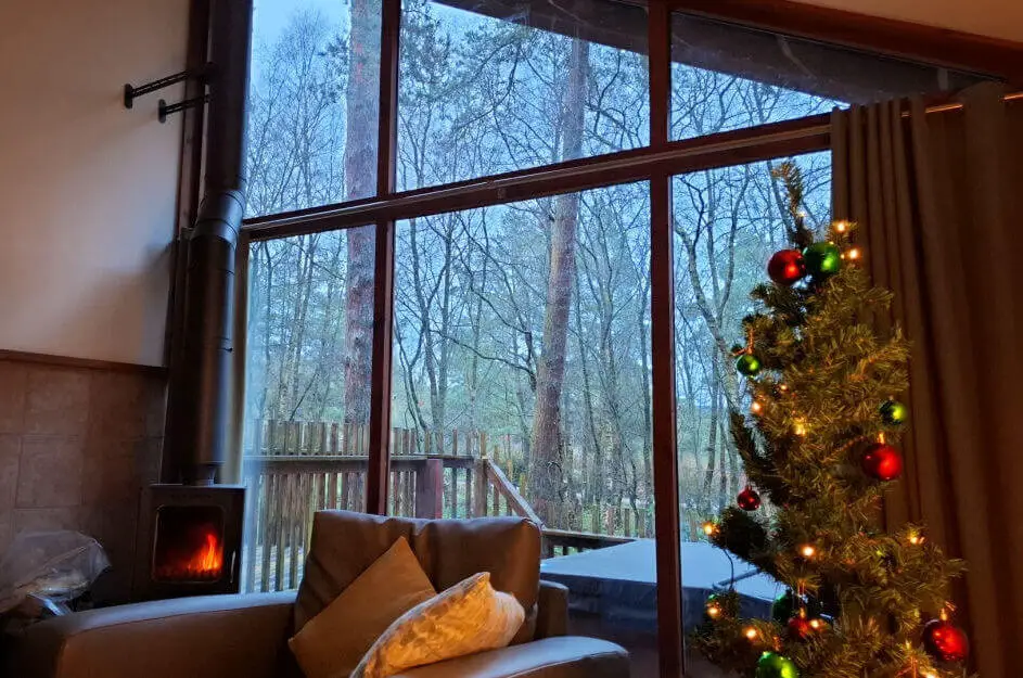 A view across a living room showing a cosy armchair just behind, and a lit log burner in front of floor-to-ceiling windows