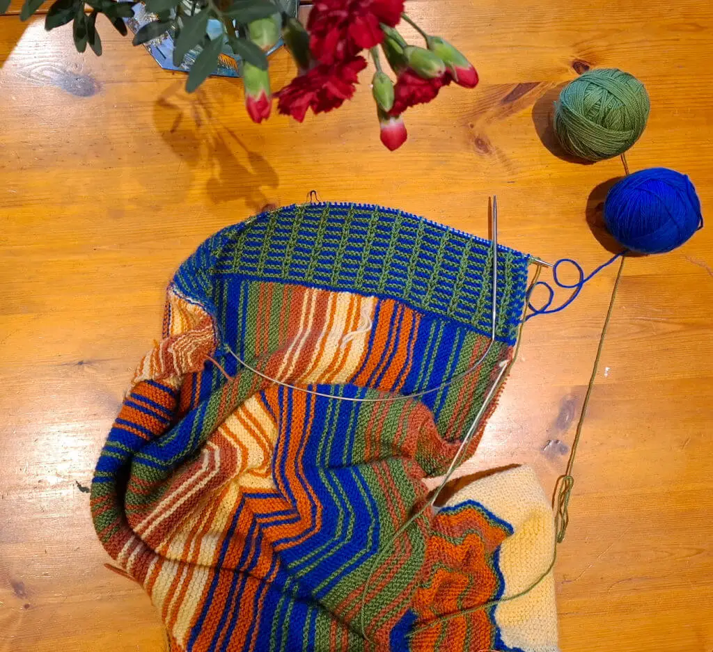 A partly-knitted shawl in blue, yellow, orange, pumpkin and green yarn