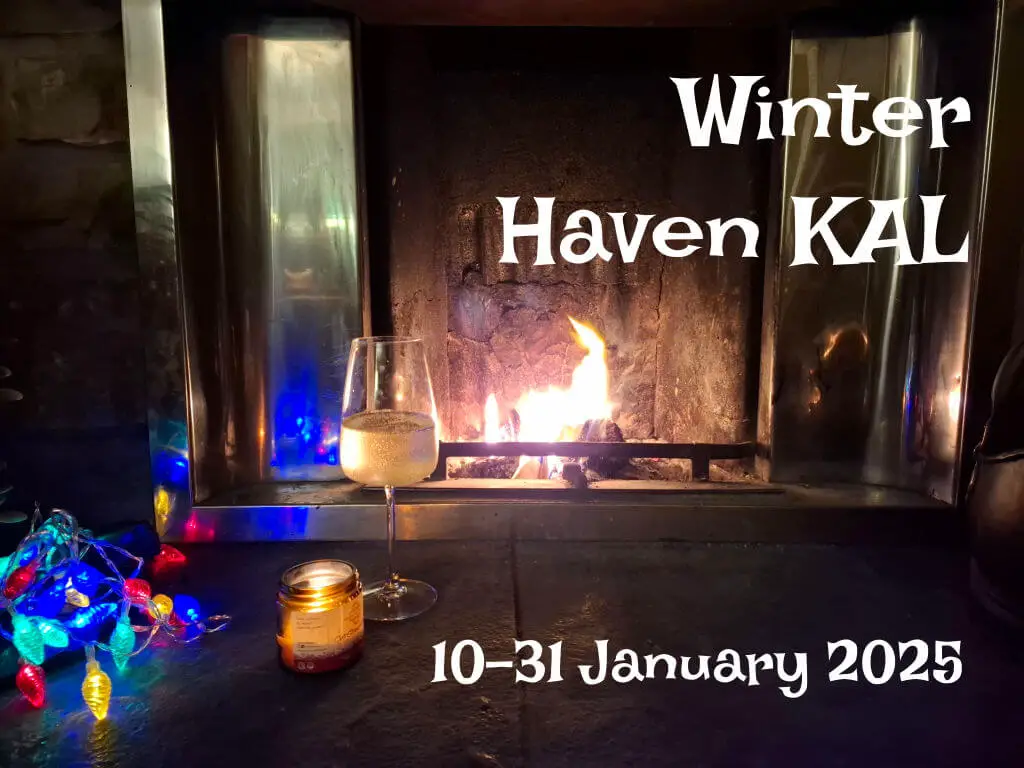 An open fire burning in a grate behind a large stone hearth with a glass of wine and a lit candle on it