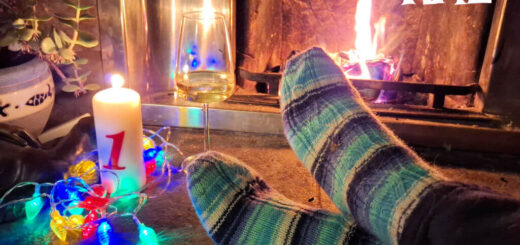 A pair of feet modelling blue and white striped socks on a stone hearth next to an open fire and a candle surrounded by fairy lights