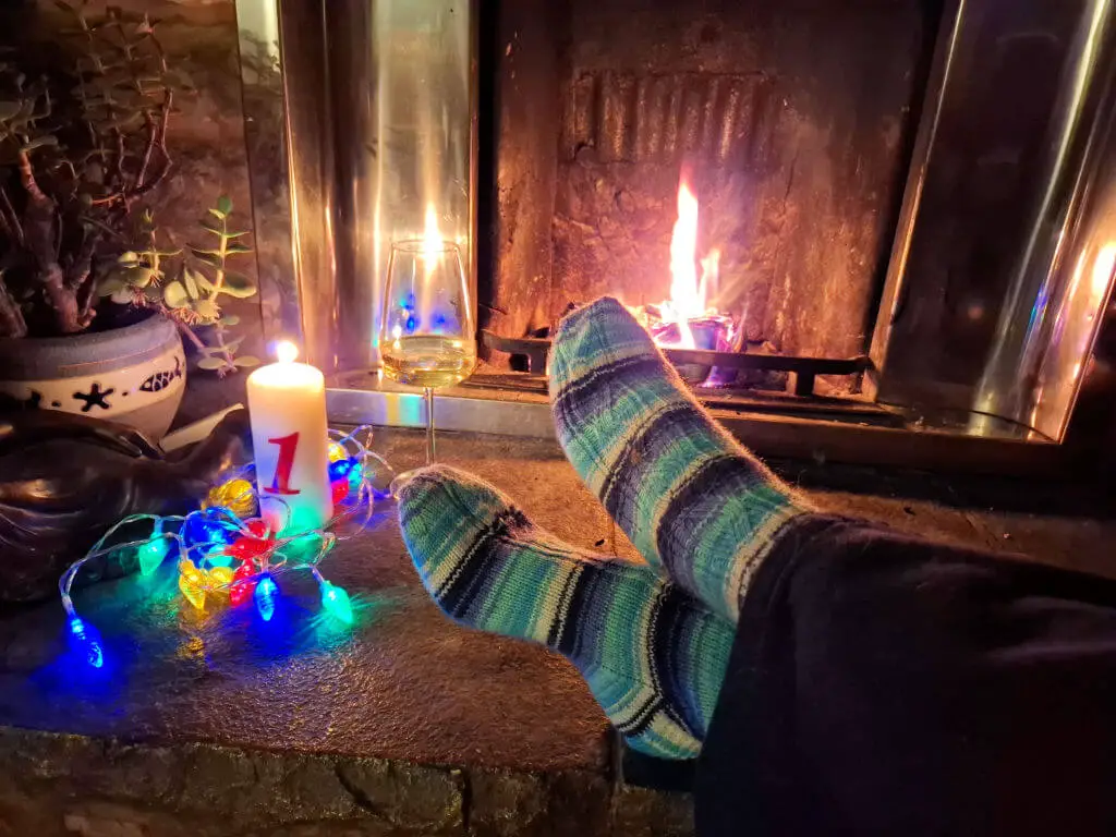 A pair of feet modelling blue and white striped socks on a stone hearth next to an open fire and a candle surrounded by fairy lights