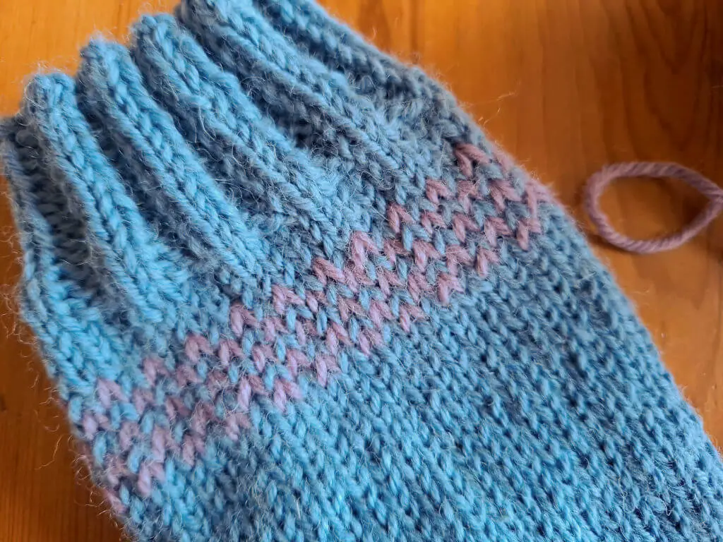 A close up of the colourwork detail on a blue and pink knitted sock