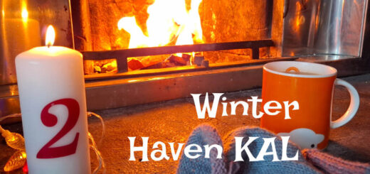 An orange mug of tea on a stone hearth next to a partly-knitted sock, a tall candle with the number 2 on it and fairy lights. There is a fire blazing in the background