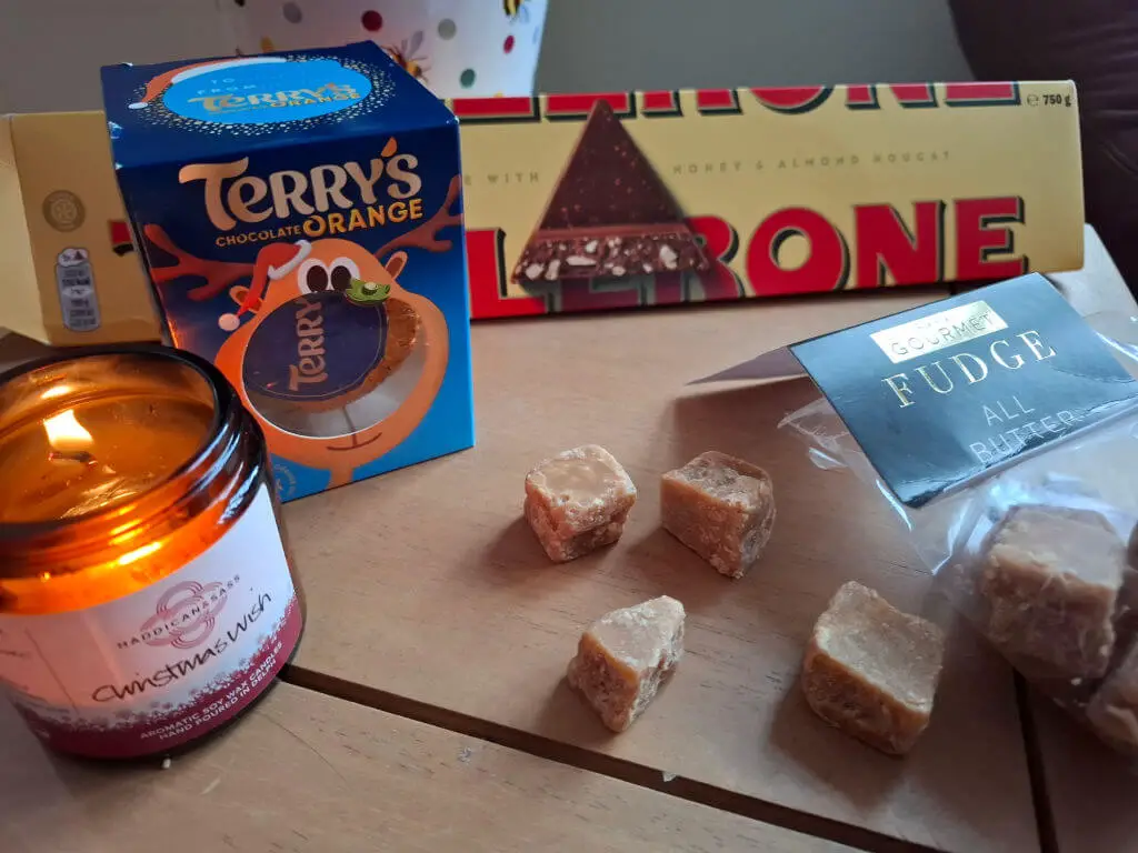 A selection of sweets and chocolate on a wooden coffee table next to a candle in a glass jar