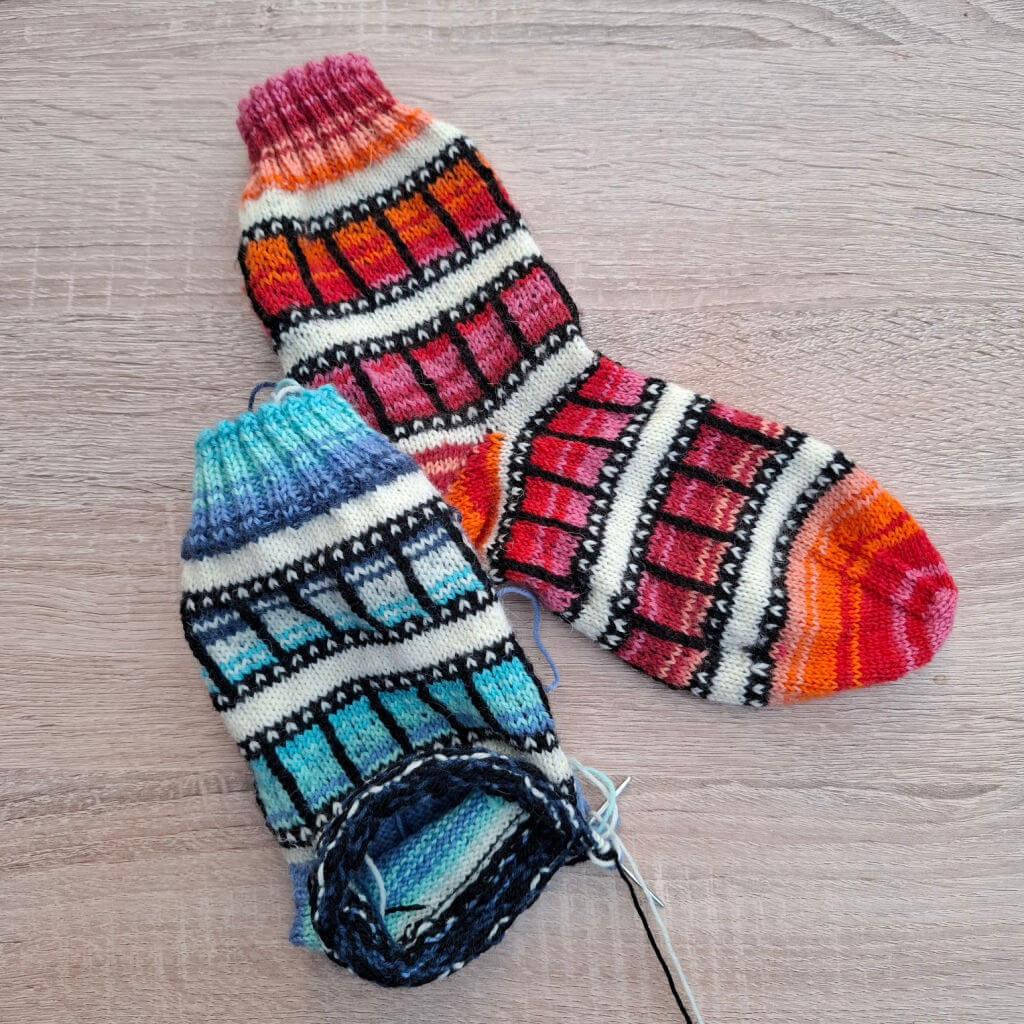 One finished and one partly-finished sock knitted to look like film reel