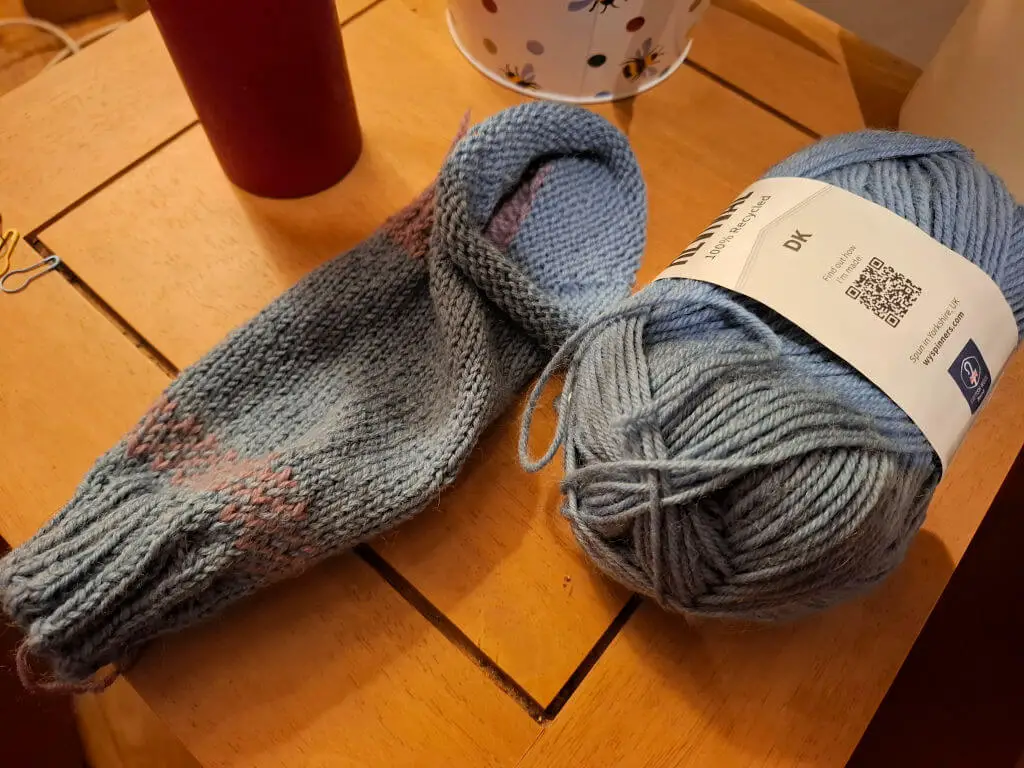 A partly knitted sock lying on a wooden coffee table next to the ball of yarn