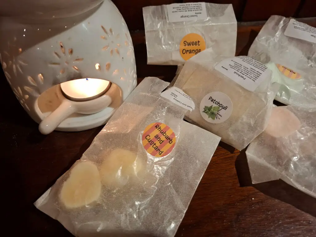 A selection of wax paper packets containing wax melts next to a wax melt burner