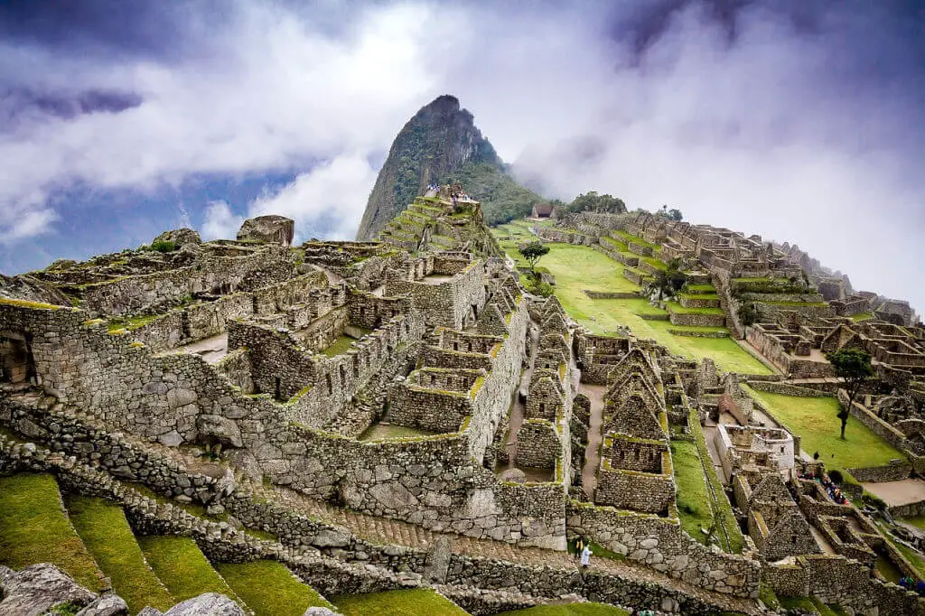 Ancient stone ruins of Machu Picchu cascade down a misty mountain landscape. Clouds envelop the peaks, conveying a mystical and serene atmosphere.