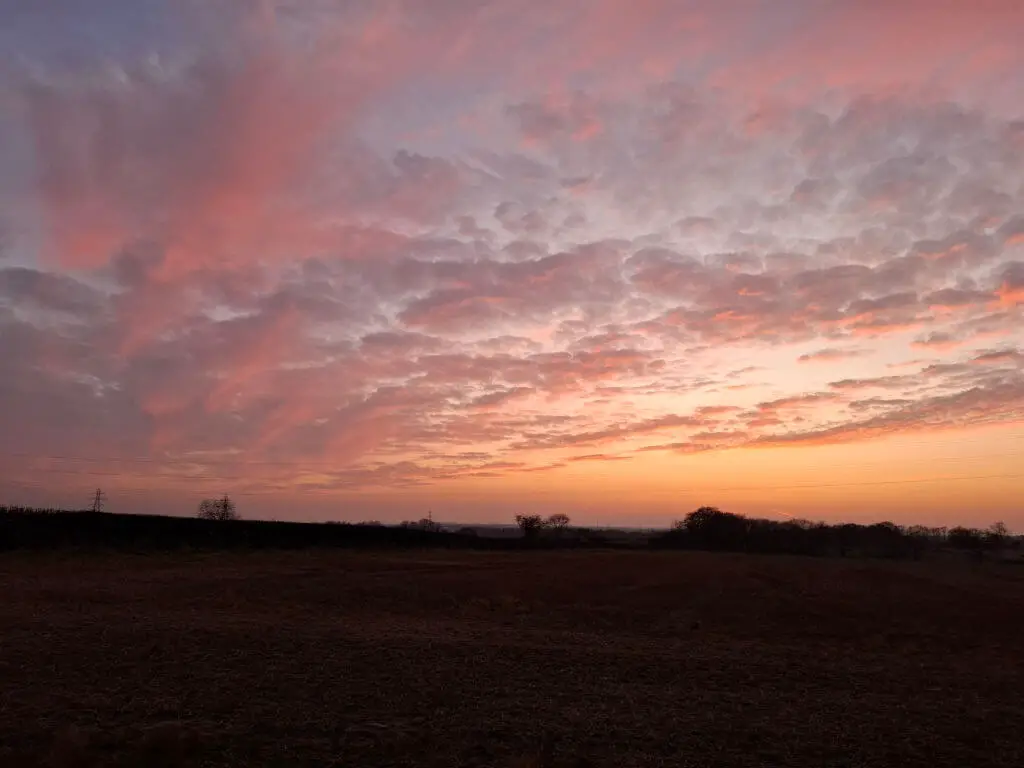 Sunset over a field with a dramatic sky filled with pink and orange clouds. The landscape is peaceful, evoking a sense of calm and tranquility.