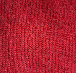 Close-up image of a red knitted fabric with a soft texture. The intricate patterns and warm tones convey a cozy, comforting feel.