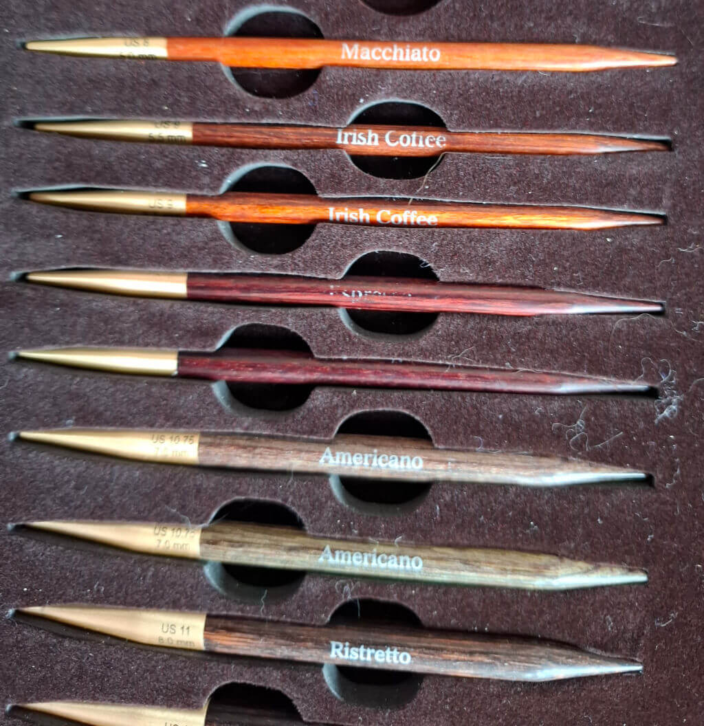 A collection of wooden knitting needles with brass tips, neatly arranged in a dark, cushioned case. Each is labeled with coffee-themed names | Winwick Mum KnitPro Knit & Sip Set Review